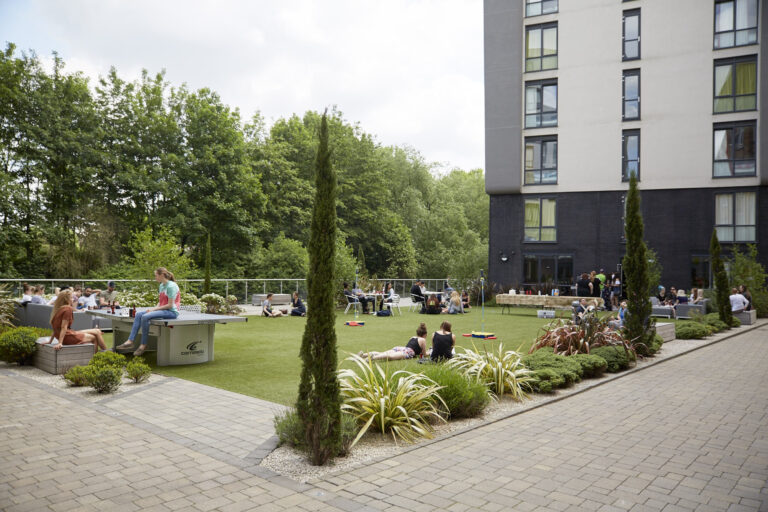 Communal outdoor space with students relaxing and socialising on the grass